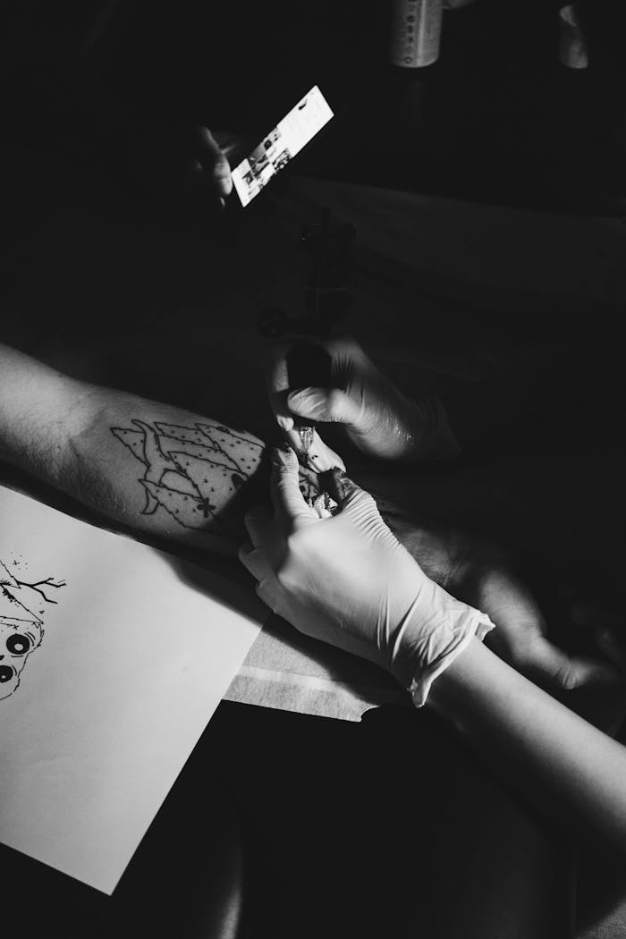 Black and white image of a tattoo artist working on a client